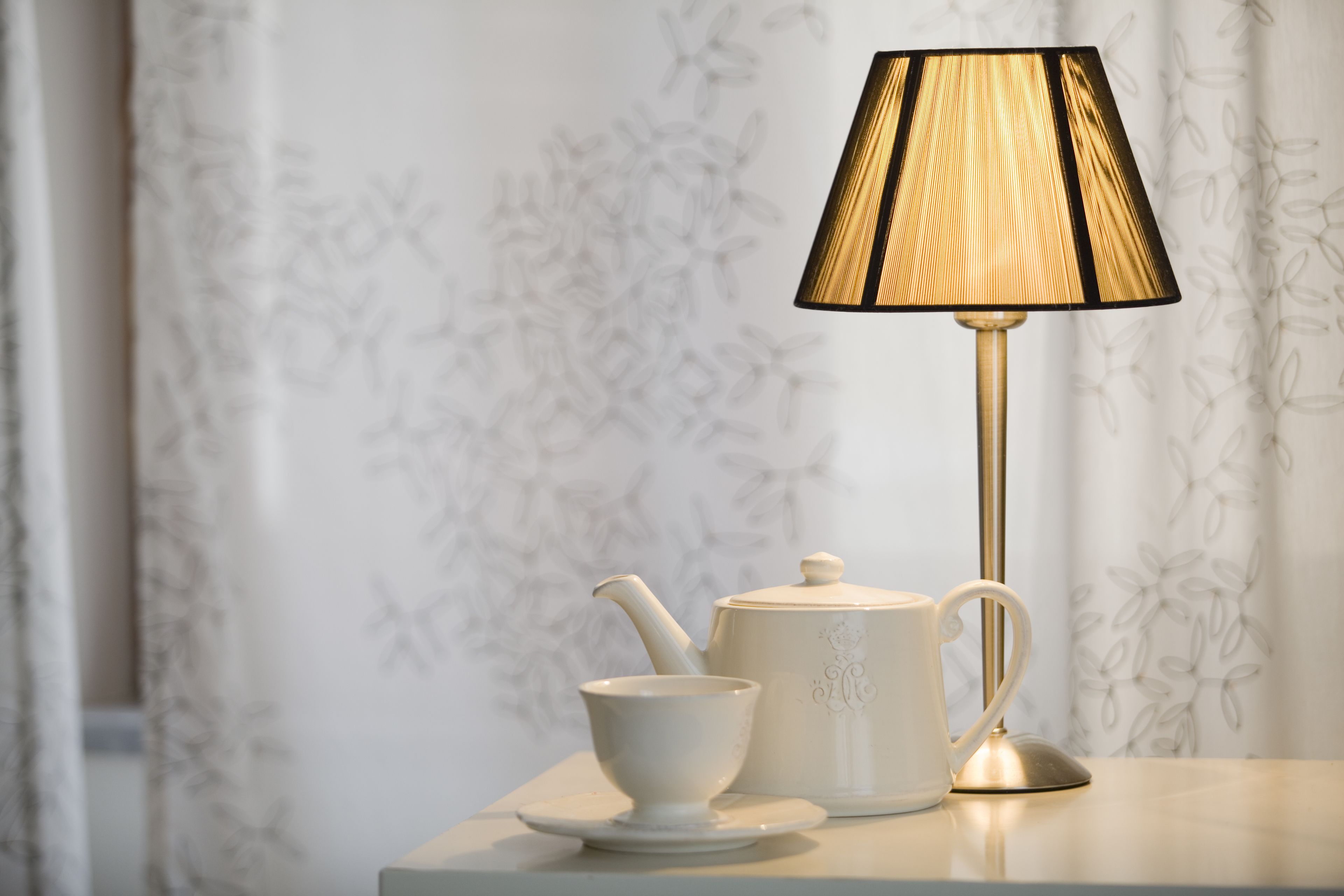 A white teapot and cup set on a table with a lamp.