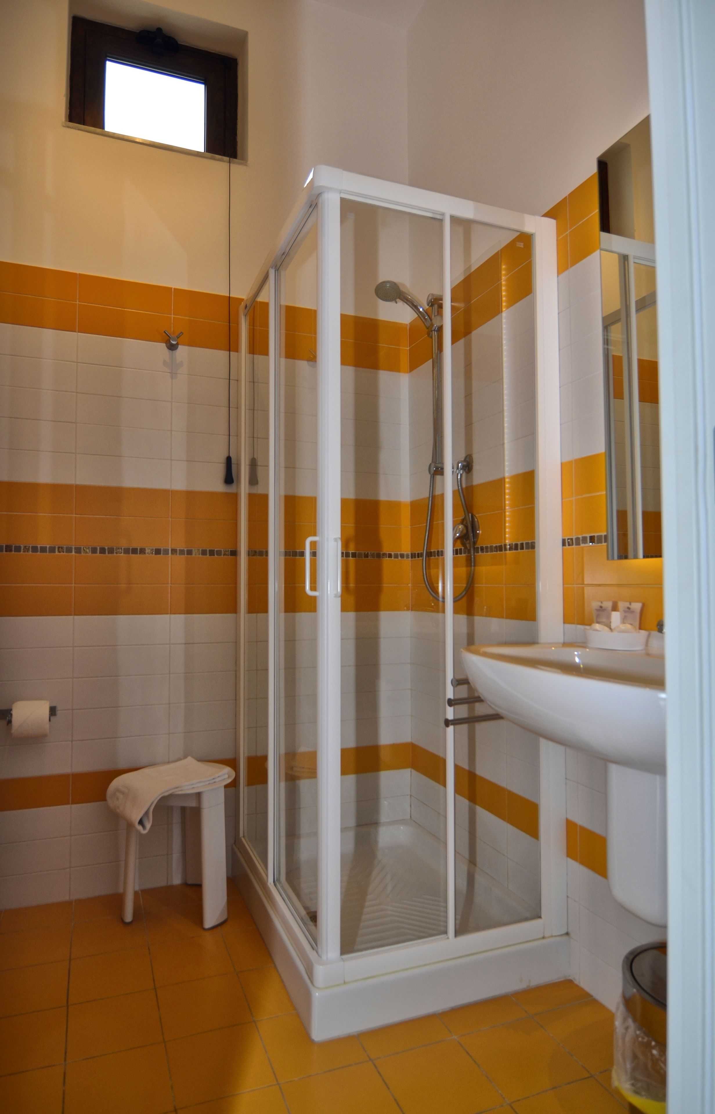 Een badkamer met een douche met glazen wand, een witte wastafel en een klein krukje.