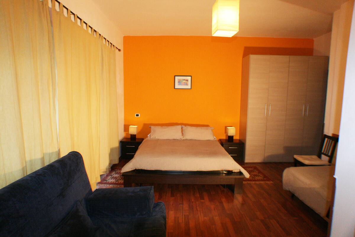A bedroom with a bed, a nightstand, a chair, a wardrobe, and a window with curtains.