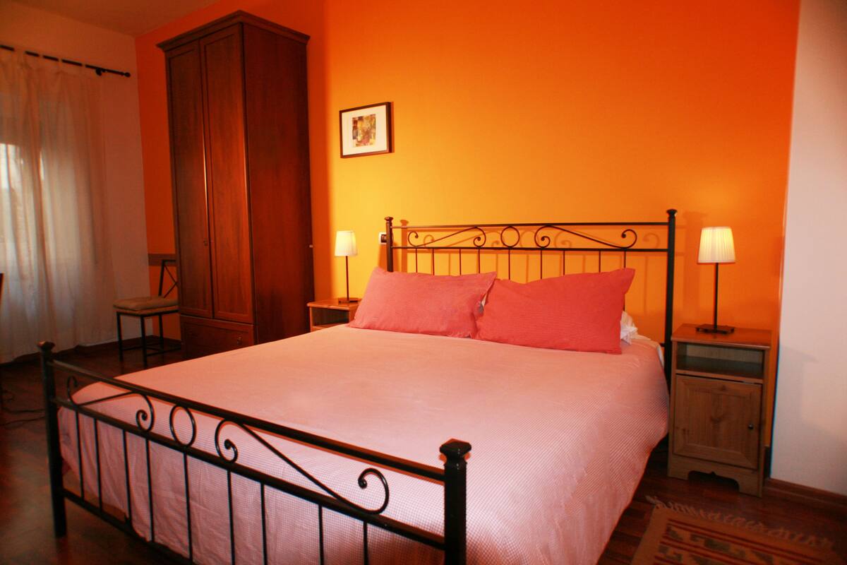 A neatly made bed with a metal frame, two bedside tables with lamps, a wooden wardrobe, and a framed picture on the wall.