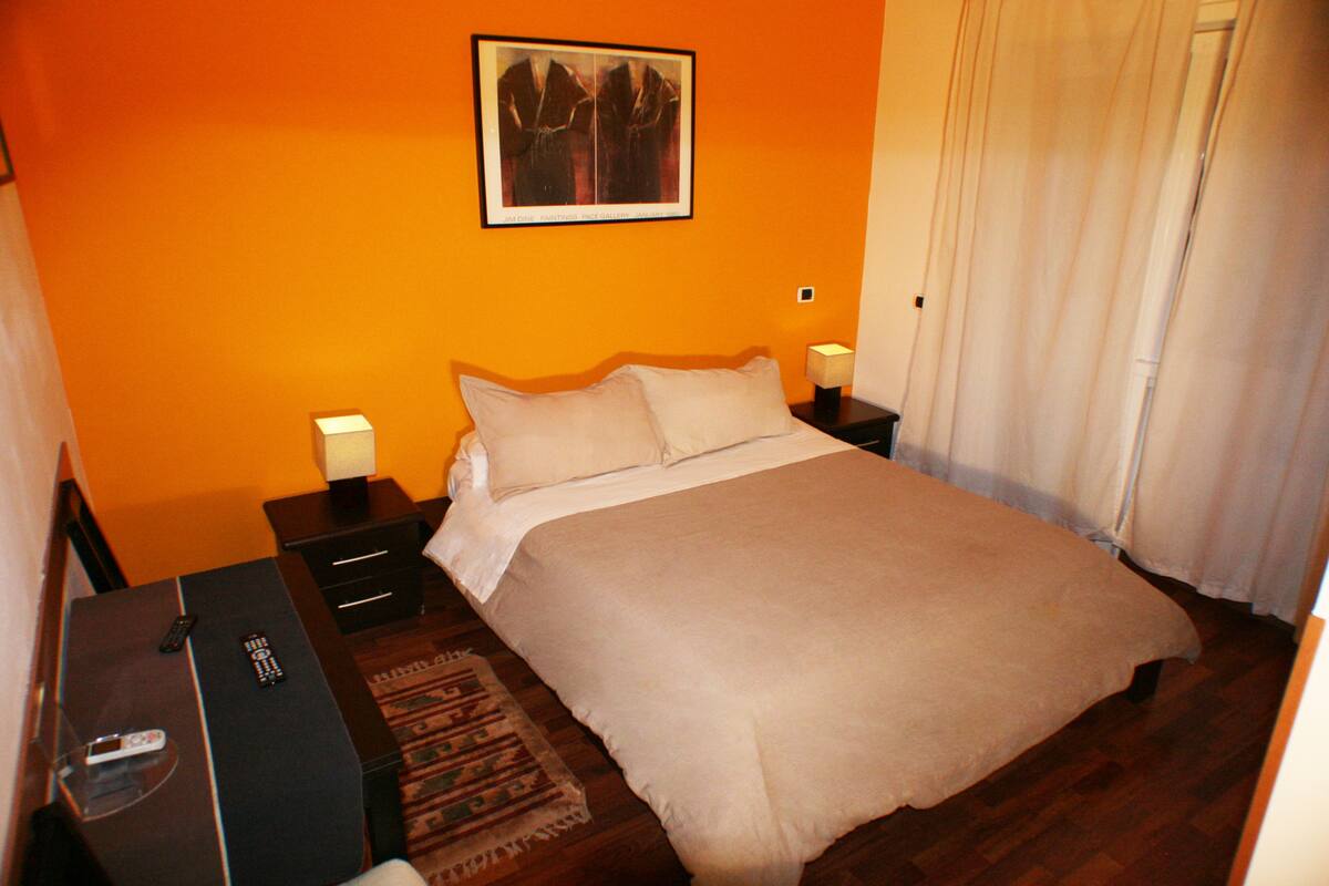 A bedroom with a bed, nightstands, and a remote control on a desk.