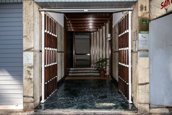 A hallway with a marble floor leading to a door. There is a potted plant on the right side. - B&B Santa Croce (Rome)
