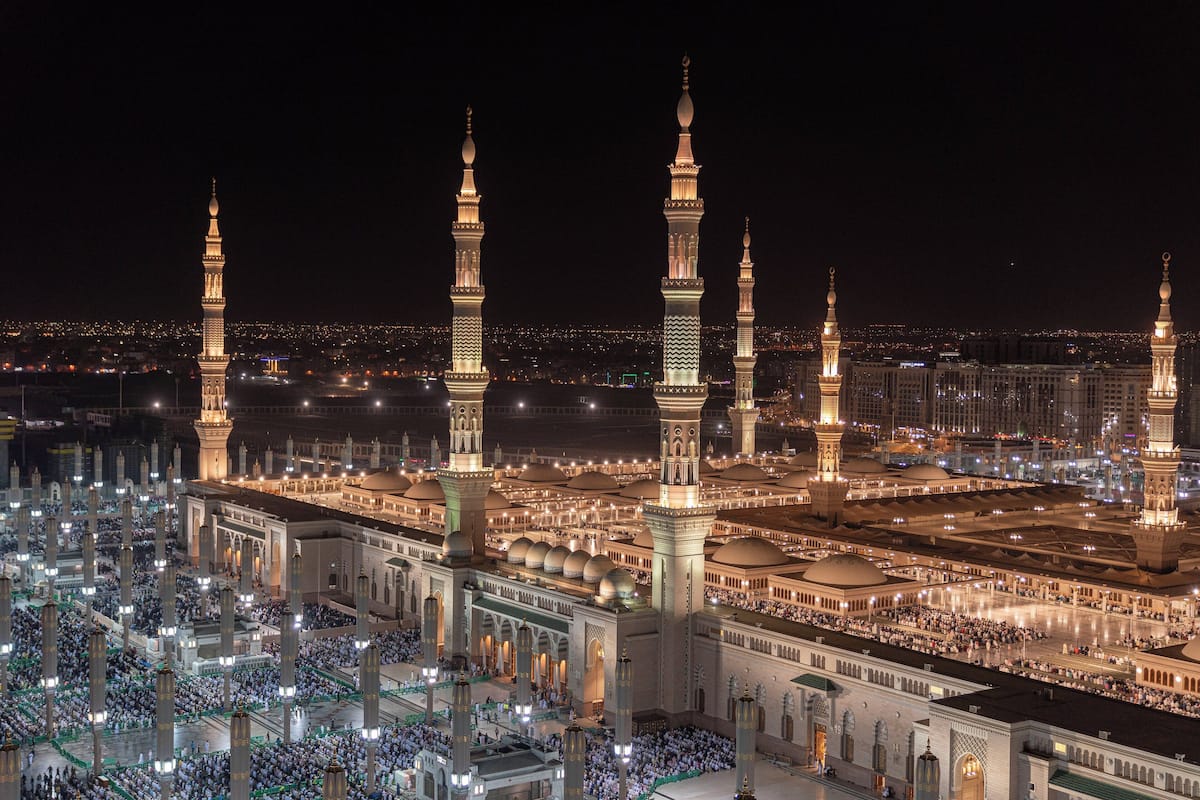 Eine große Moschee mit mehreren Minaretten und einem weitläufigen Innenhof voller Menschen.