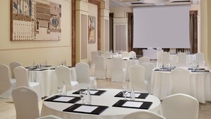 A conference room with round tables, white chairs, and a large screen for presentations. - Intercontinental Madinah - Dar Al Iman by IHG (Madinah)