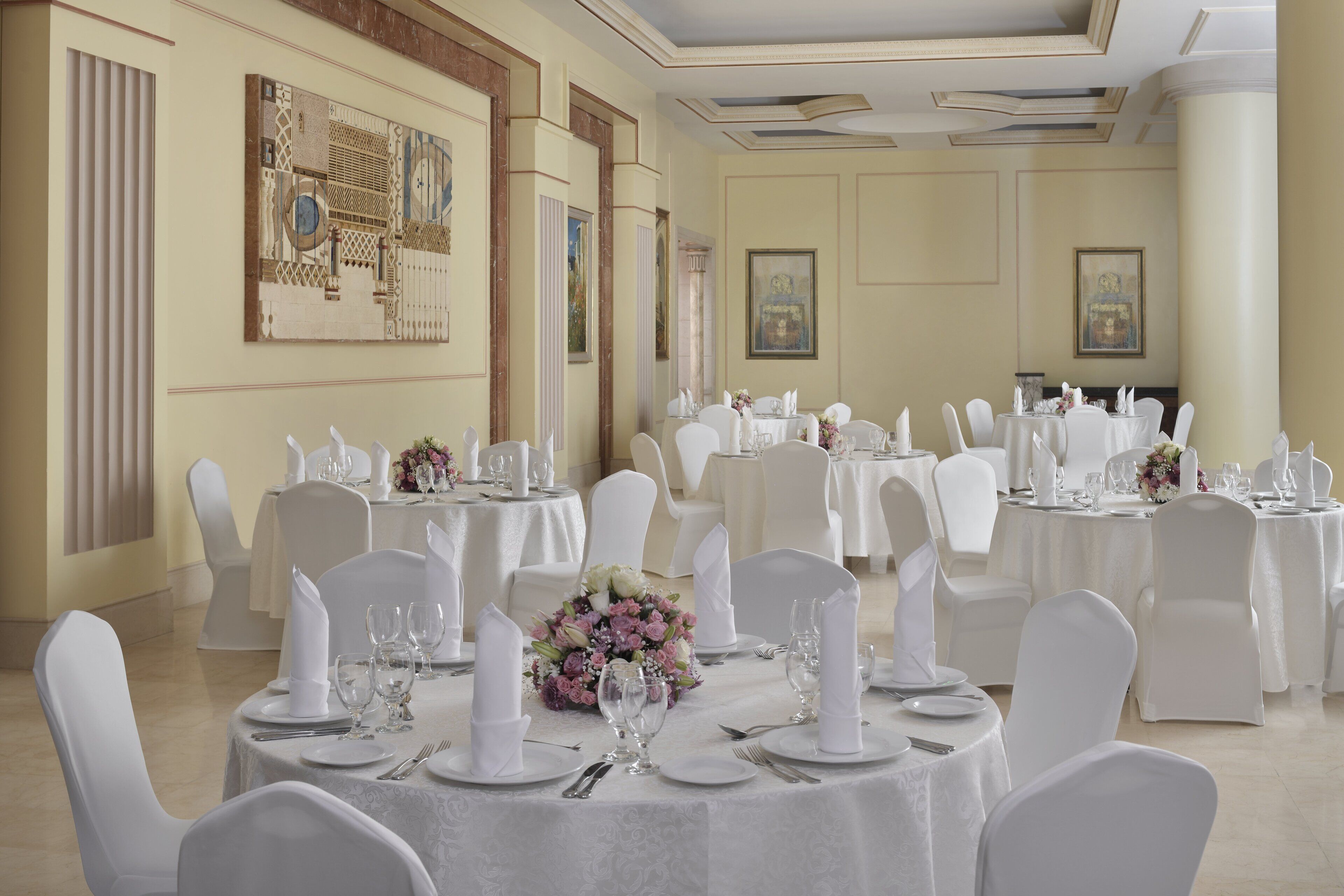 A banquet hall with round tables set for dining, white chairs, and floral centerpieces.