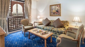 Una habitación con alfombra azul estampada, un sofá con cojines estampados, una mesa de centro de madera y vistas a través de un ventanal decorativo.