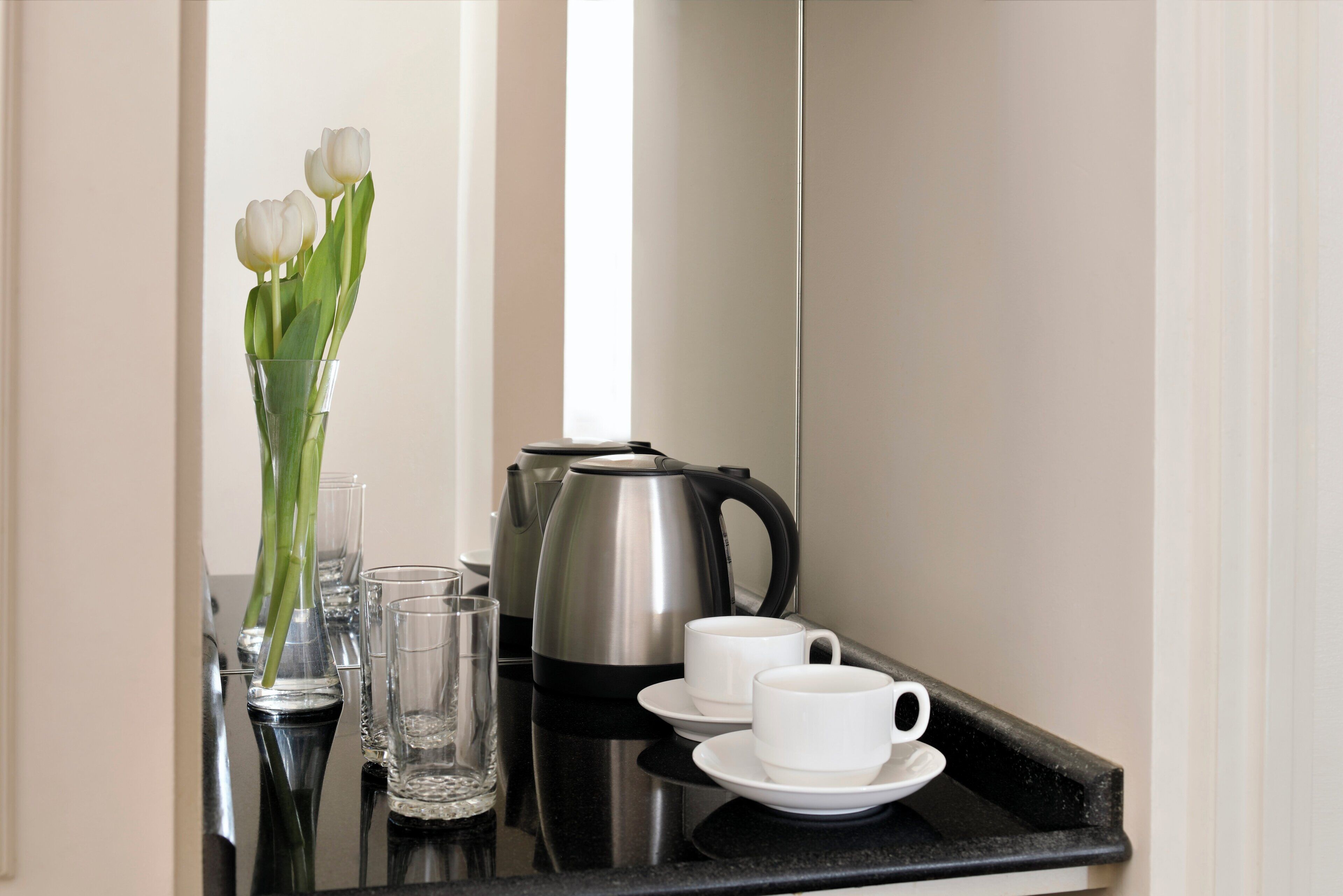 A kitchen counter with a coffee maker, two white cups, and a vase with white flowers.