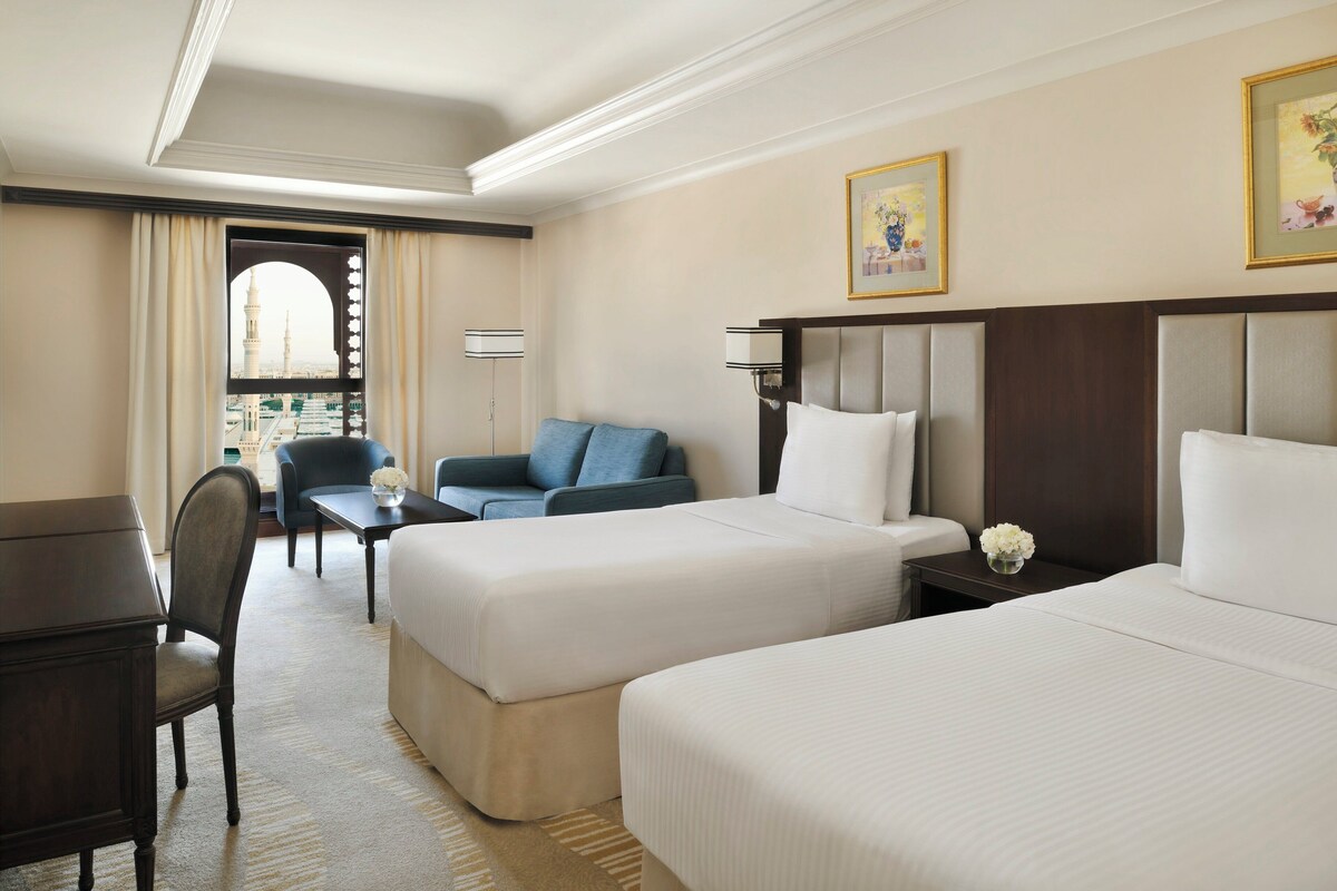 A hotel room with two beds, a desk, a chair, and a sofa.