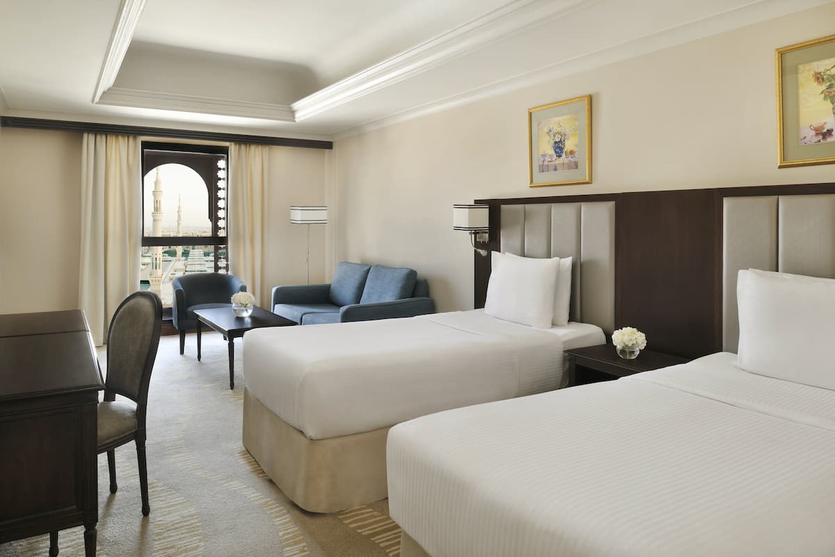Ein Hotelzimmer mit zwei Betten, einem Schreibtisch, einem Sessel und einer Couch.