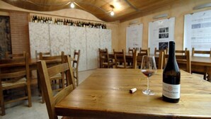 A wooden table with a wine bottle and glass, surrounded by wooden chairs in a room with a brick wall and posters on the wall. - Hotel Borghetti (Verona)