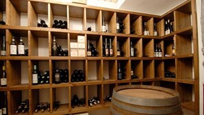 A wine cellar with wooden shelves filled with wine bottles and a large wooden barrel. - Hotel Borghetti (Verona)