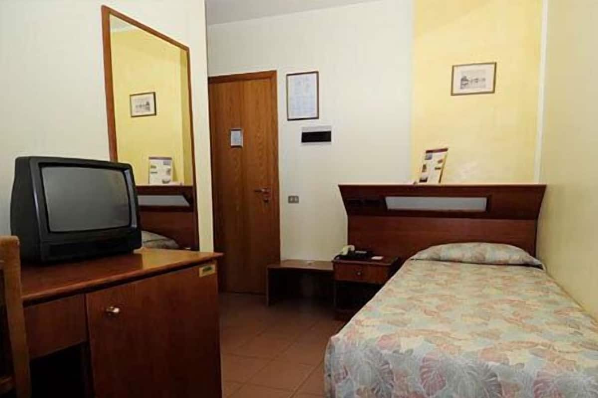 Una habitación de hotel con una cama, un escritorio con televisor, una mesita de noche y una puerta.