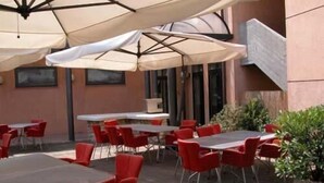 An outdoor patio with tables and red chairs, covered by umbrellas. - Hotel Borghetti (Verona)