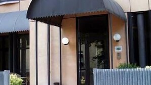 A building with a black awning over the entrance, a visible door, and a small outdoor seating area with planters. - Hotel Borghetti (Verona)