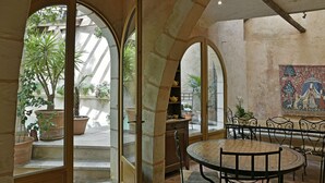 A room with a round table and chairs, a view of the courtyard through an arched doorway, and a mosaic on the wall. - Un Mas en Ville (Marseille)