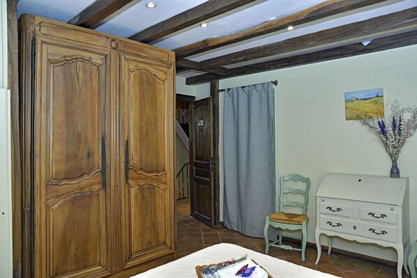 A room with a wooden wardrobe, a white dresser, a chair, and a painting on the wall.