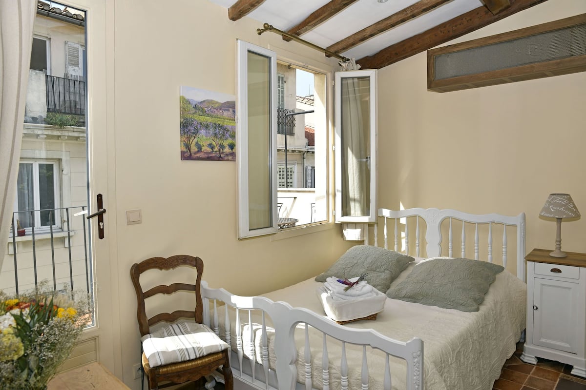A bedroom with a bed, a chair, a bedside table, and a window.