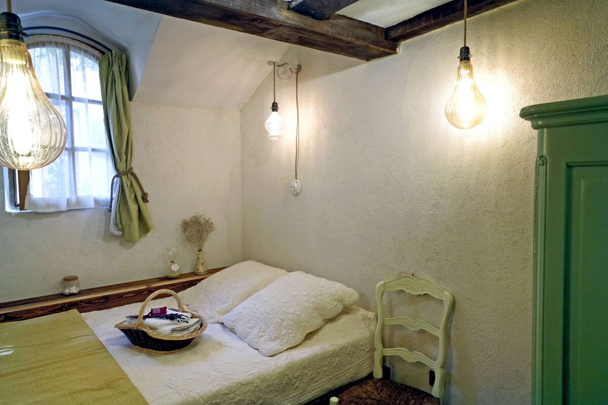 A cozy bedroom with a bed, a nightstand, a lamp, and a window with curtains.