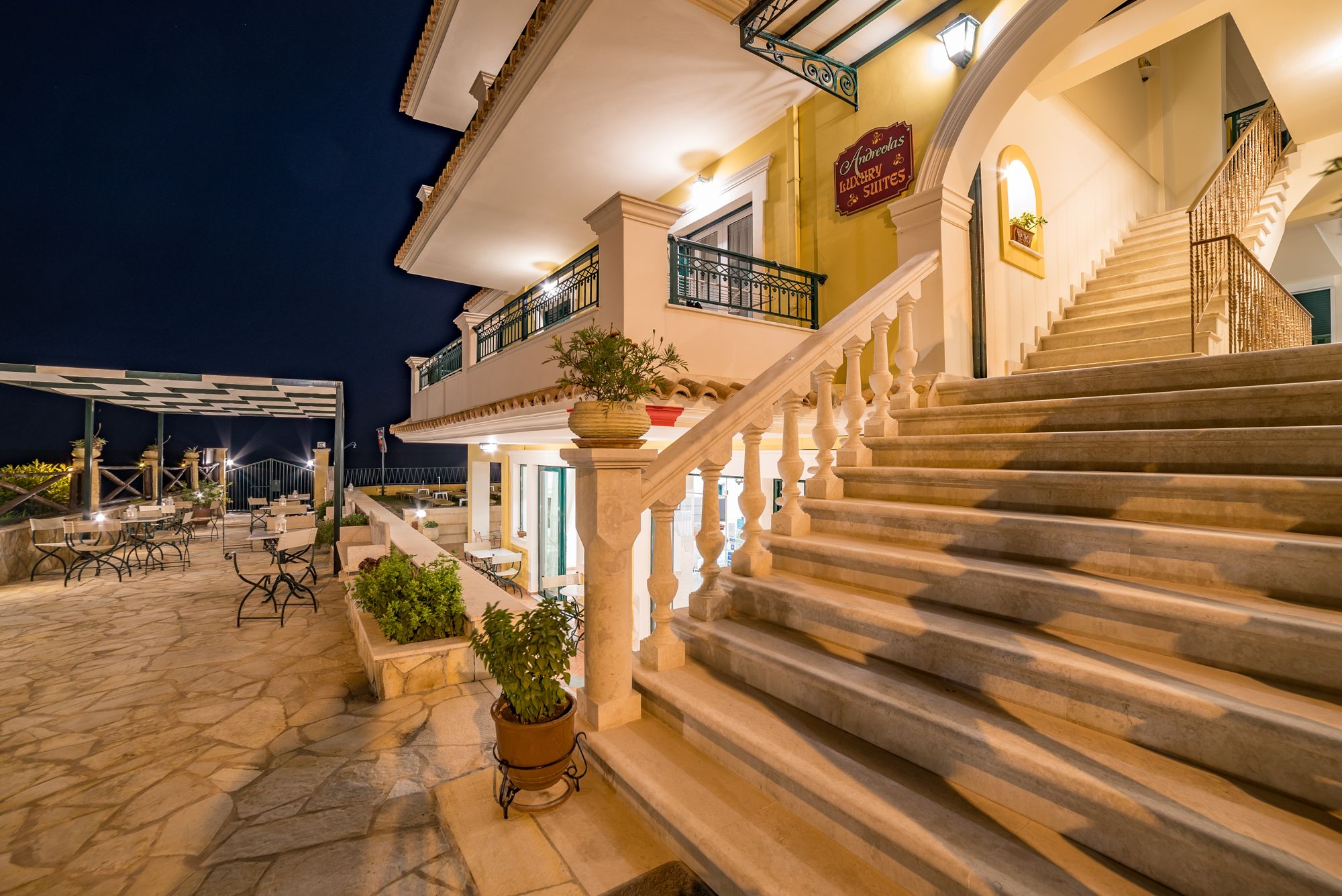 A hotel exterior with outdoor seating, a staircase, and a sign for "Anvelgas Luxury Suites".