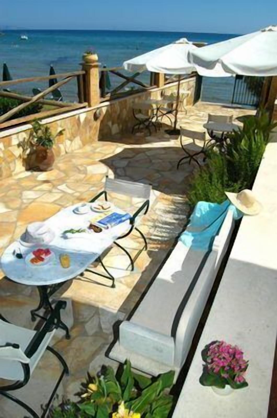 An outdoor patio with stone flooring, white tables and chairs, and umbrellas.