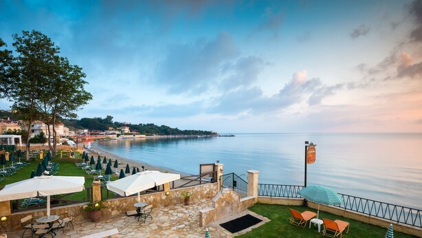 Un patio de hotel frente al mar con mesas al aire libre, un muro de piedra y vistas panorámicas.