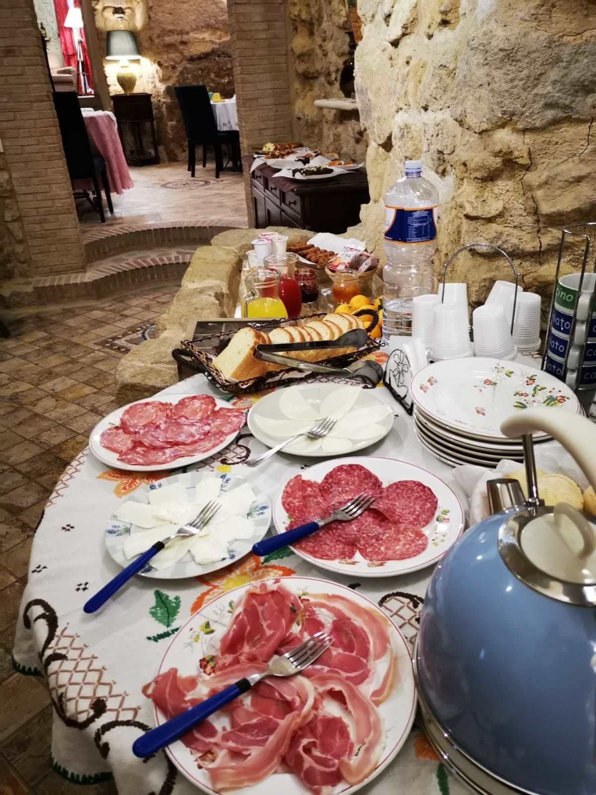 Un bufé de desayuno con diversas carnes, quesos y frutas, frente a una rústica pared de piedra.