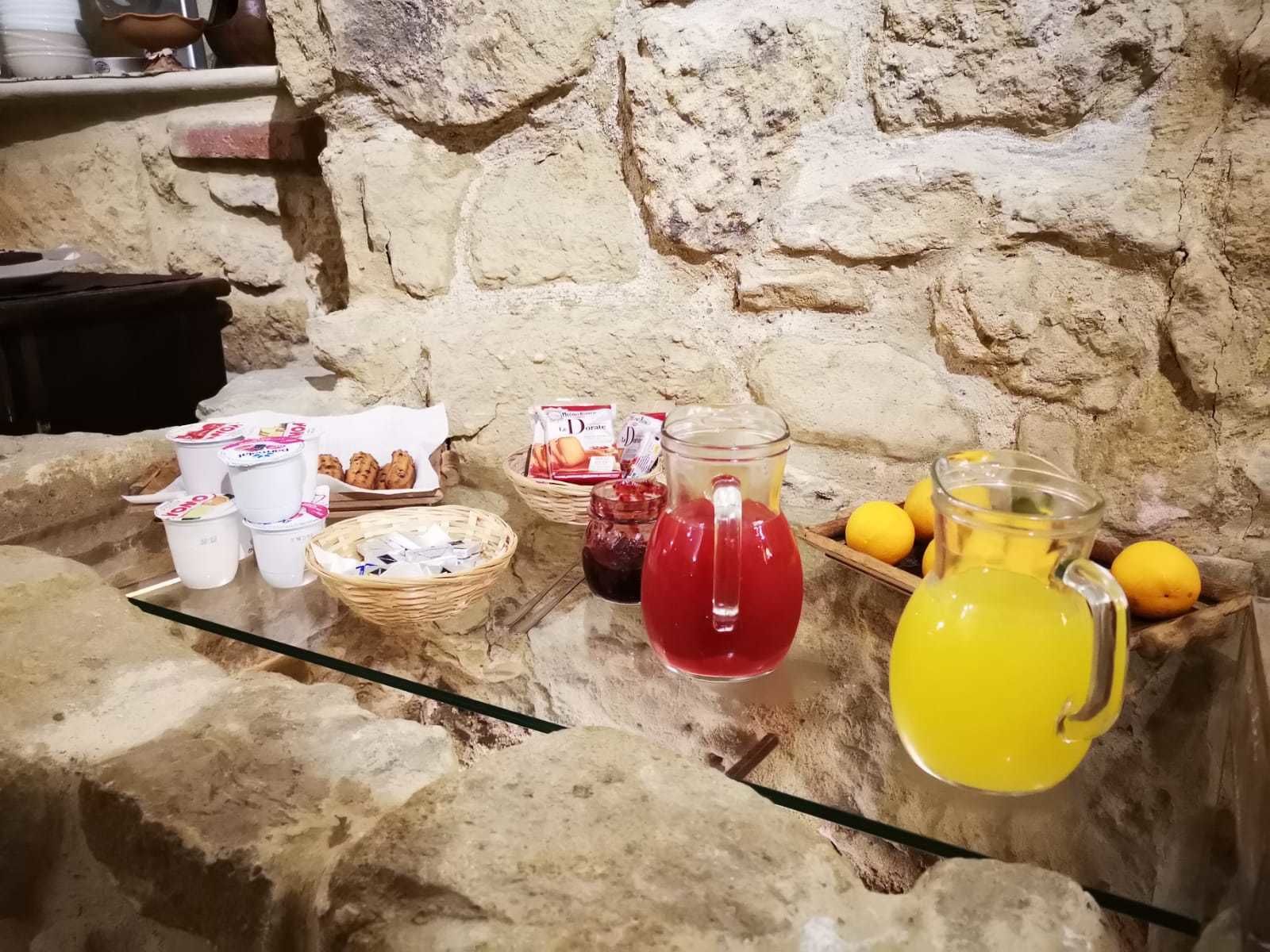 A stone wall with various food items and drinks on a glass table.