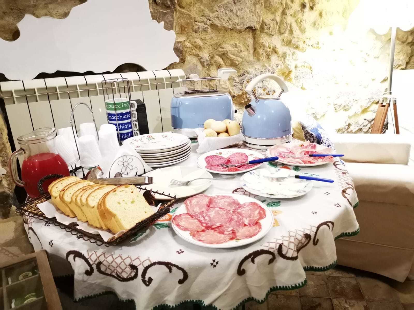 A breakfast table with bread, plates of meat, and a coffee maker.