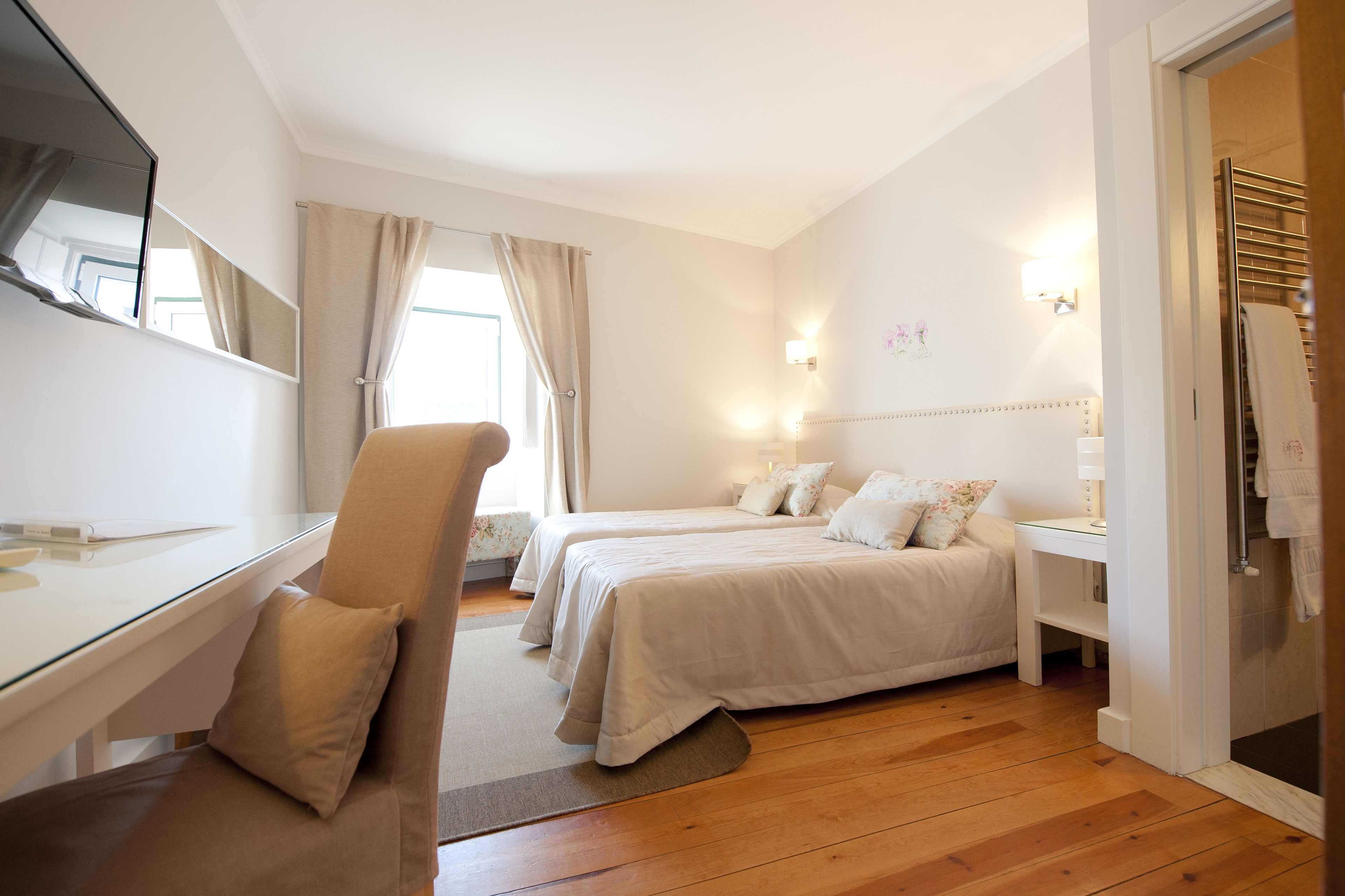 A hotel room with two beds, a desk, a chair, and a shower area.