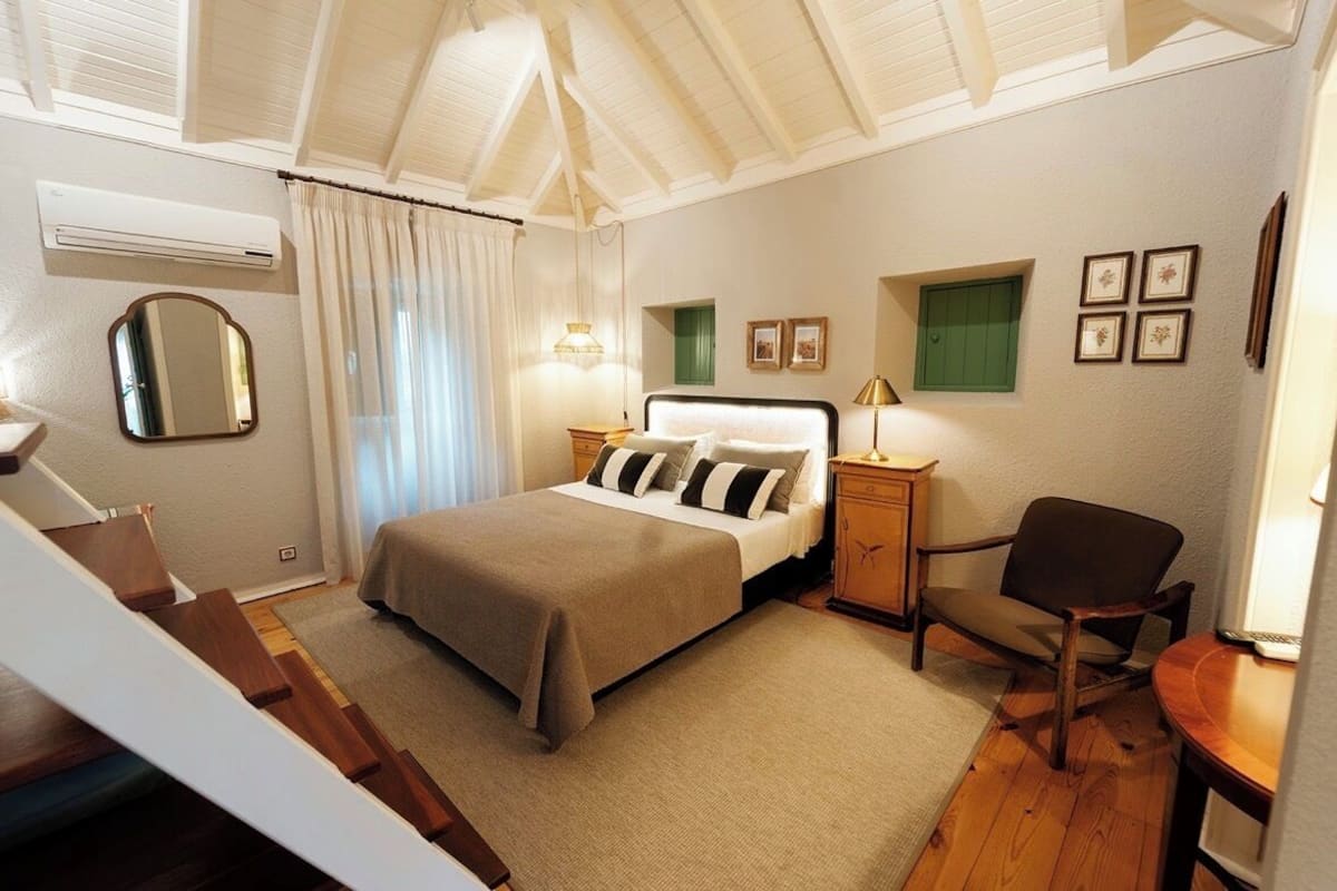 Ein Schlafzimmer mit Bett, Nachttischen, einem Sessel, einem Spiegel und einem Fenster mit Vorhängen.