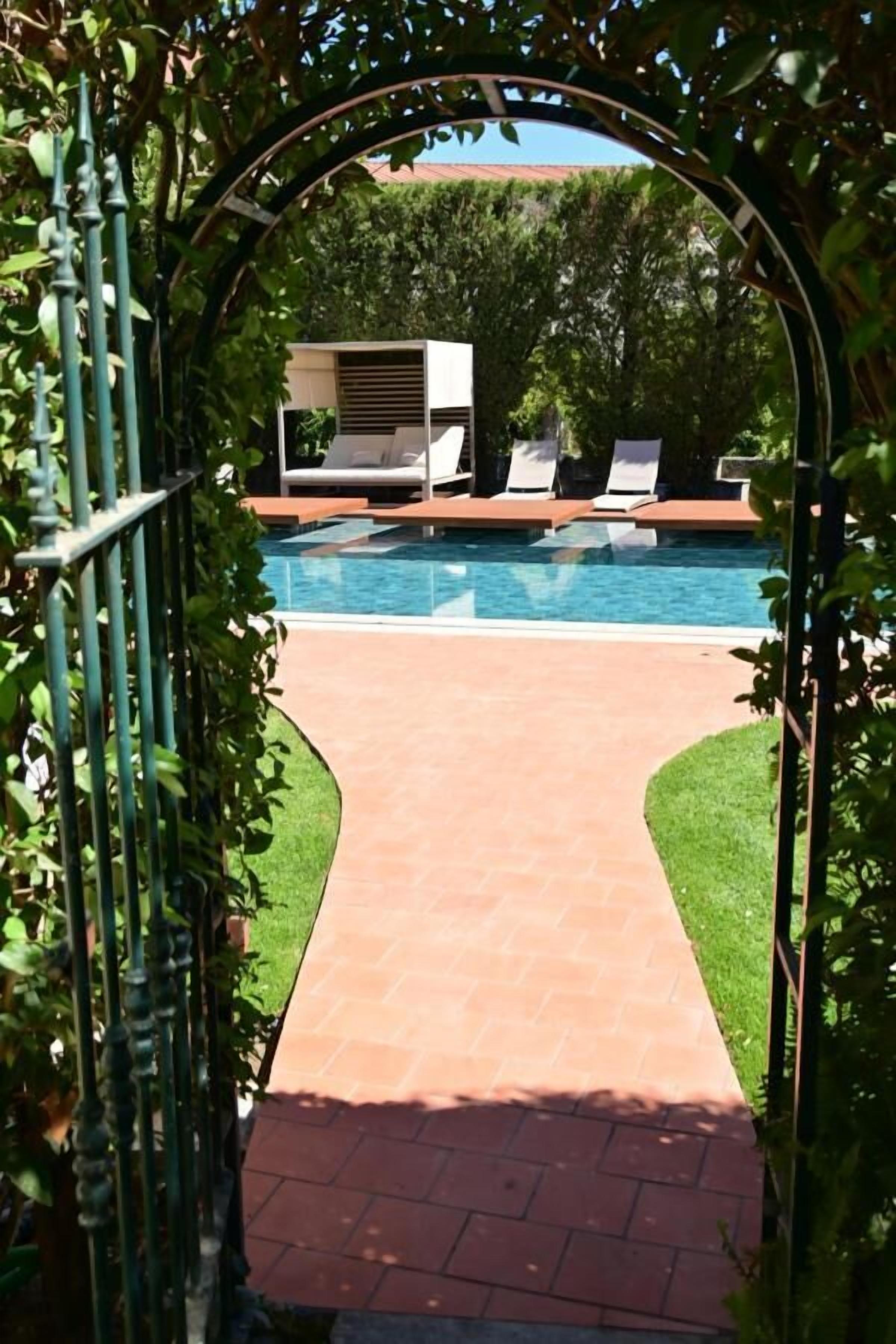 A pathway leading to a pool area with lounge chairs and a pergola.