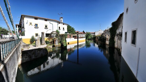 A canal with buildings on either side, a bridge, and a clear blue sky. - Hotel Casa da Nora (Leiria)