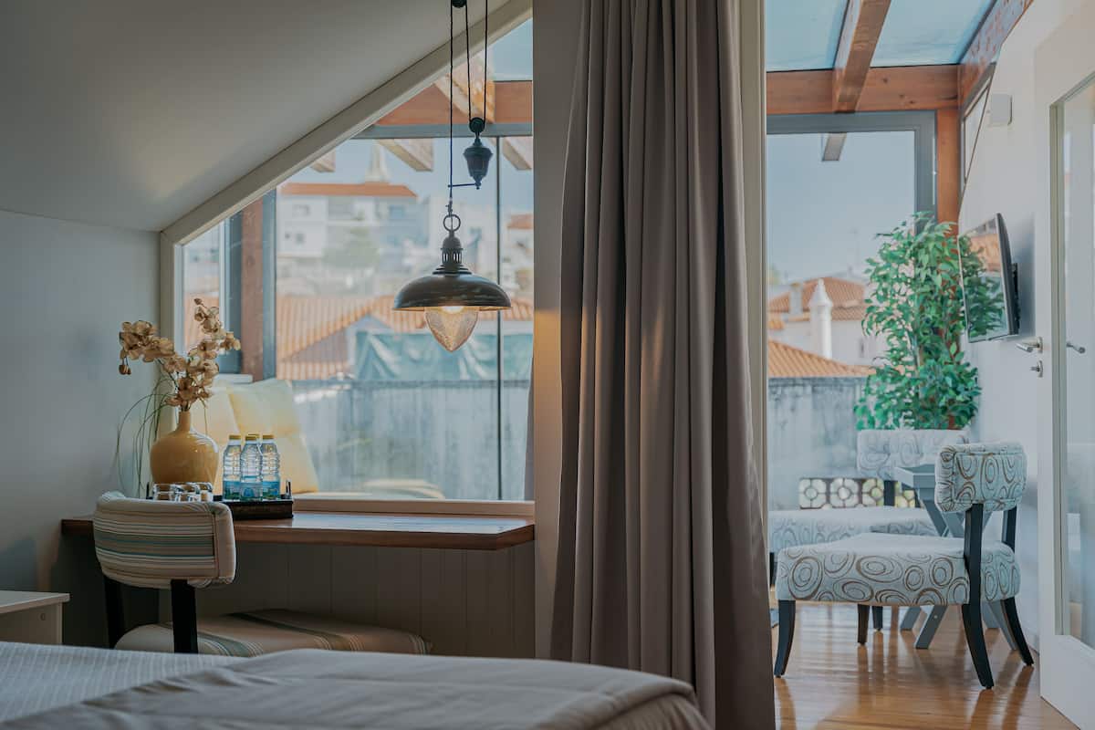 Ein Schlafzimmer mit großem Fenster, einer Pendelleuchte, einem Nachttisch mit Vase und Flaschen sowie einem Bett.