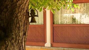 Un banco bajo un árbol, con una campana y una estructura de celosía al fondo.