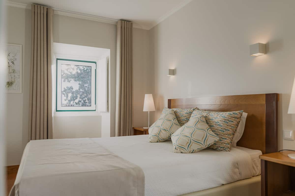 Ein Hotelzimmer mit einem großen Bett, einem Nachttisch, einer Lampe, einem gerahmten Bild und einem fenster mit Vorhängen.