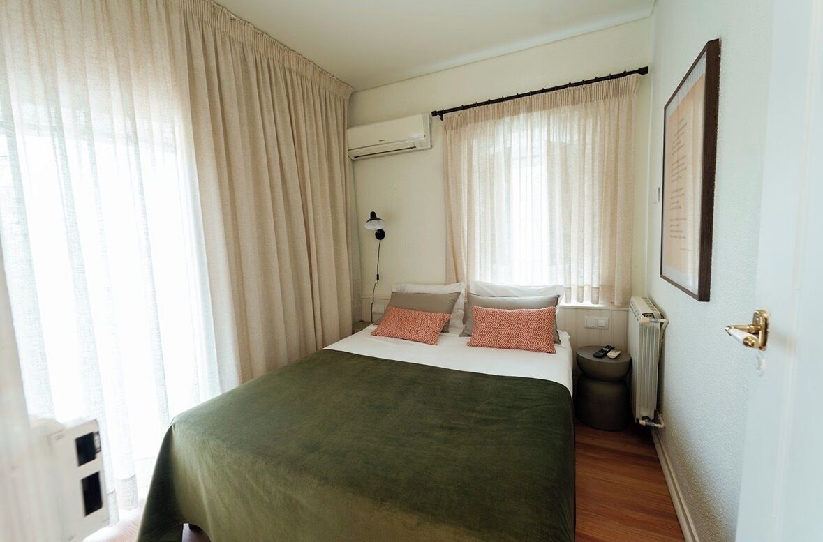 A bedroom with a bed, curtains, an air conditioning unit, a radiator, and a framed picture on the wall.