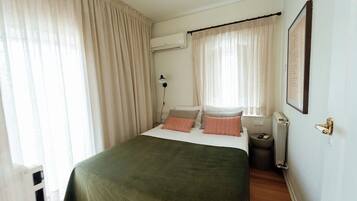 Une chambre à coucher avec un lit, des rideaux, un appareil de climatisation, un radiateur et un tableau encadré au mur.
