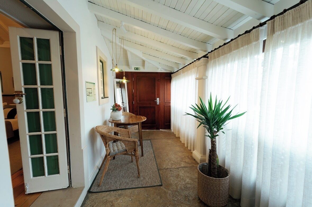 A hallway with a wooden door, a wicker chair, a small table with a vase, a potted plant, and a wooden cabinet.