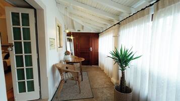 A hallway with a wooden door, a wicker chair, a small table with a vase, a potted plant, and a wooden cabinet.