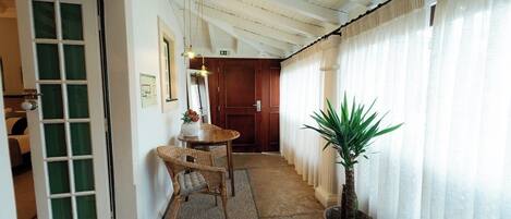 A hallway with a wooden door, a wicker chair, a small table with a vase, a potted plant, and a wooden cabinet.