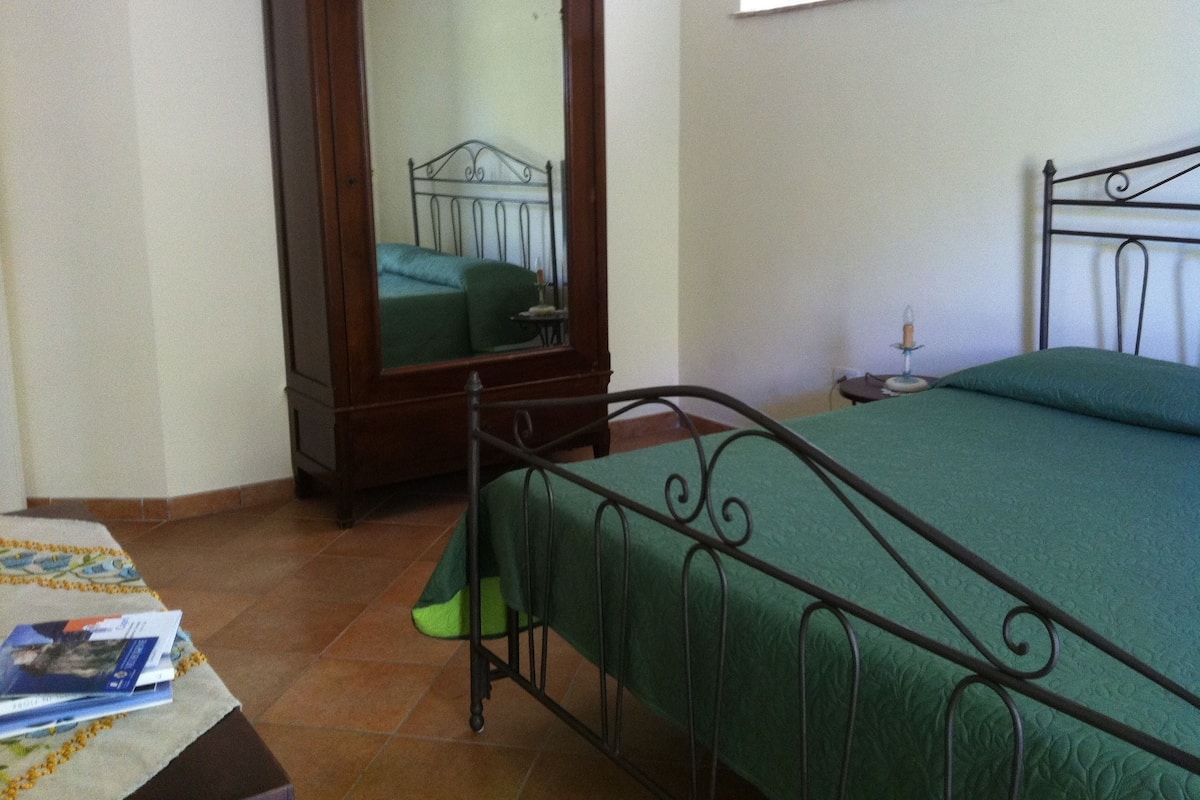 Un dormitorio con una cama, un armario de madera, un espejo y una mesita de noche con una lámpara.