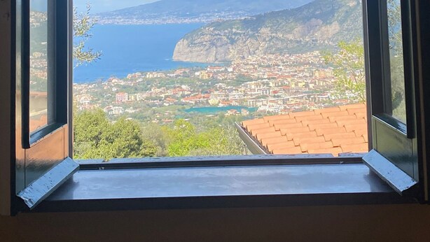 A view from a window overlooking a coastal town with a mountain in the background.