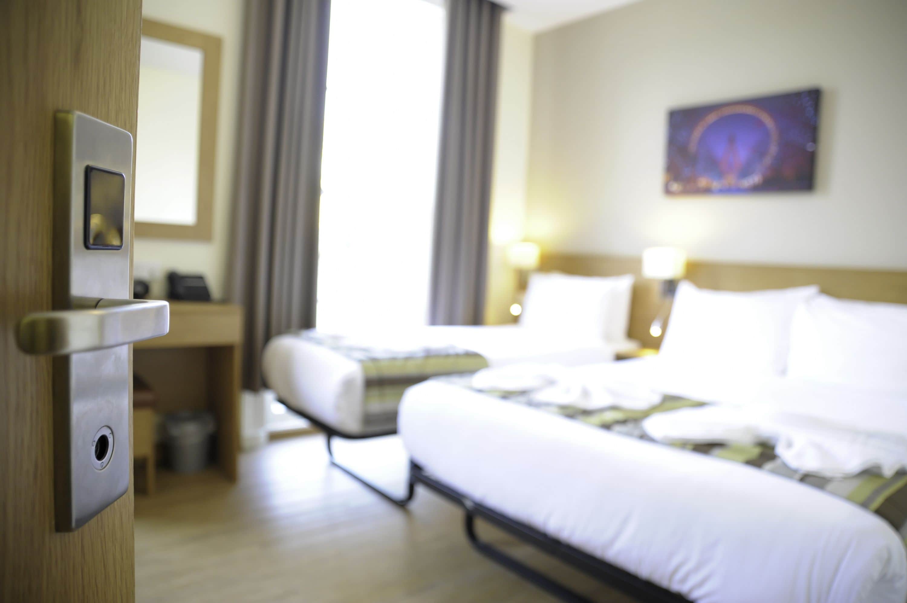 A hotel room with a bed, a bedside table, a mirror, and a window with curtains.