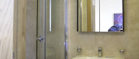 Un baño moderno con cabina de ducha de vidrio, un lavabo blanco y un mueble de tocador oscuro.
