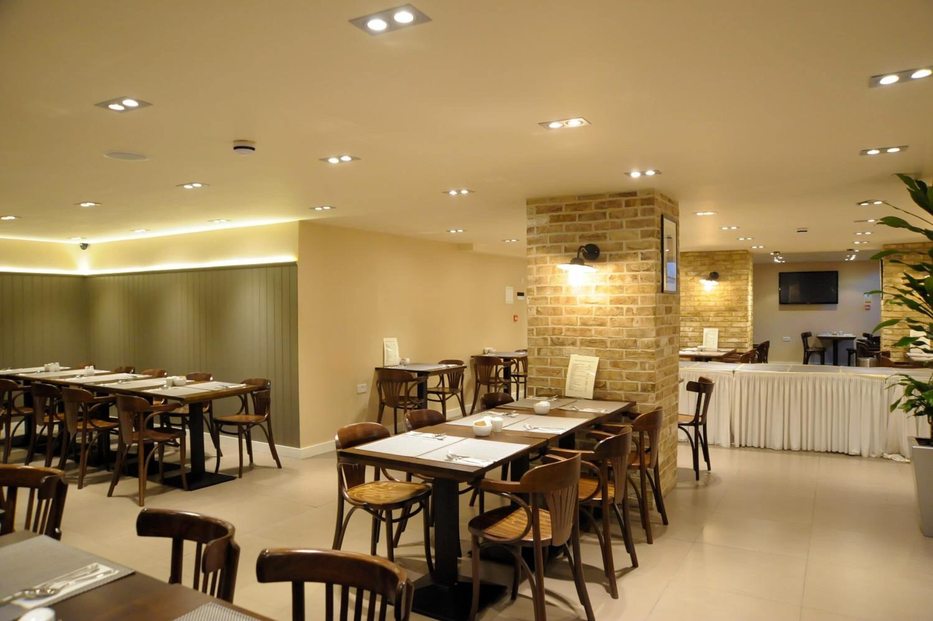 Un espace repas comprenant plusieurs tables et chaises, un mur d’accent en pierre, des spots encastrés au plafond et un téléviseur fixé au mur.