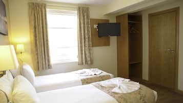 A hotel room with two beds, a TV mounted on the wall, a wardrobe, and a window with curtains.