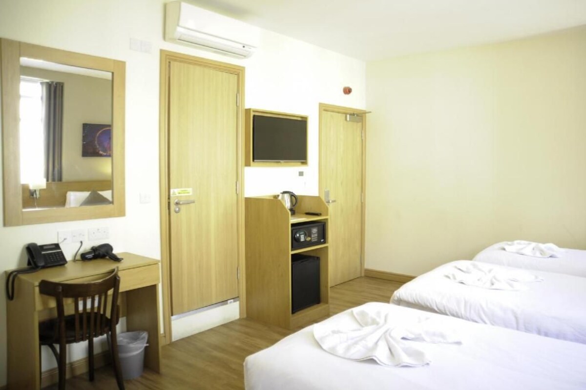 Habitación de hotel con escritorio, silla, dos camas, televisor y armario.