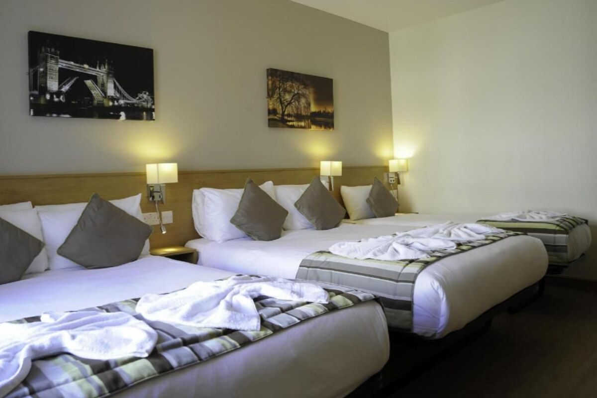 A hotel room with two beds, each with a headboard, bedside lamps, and pillows. There are wall-mounted artworks above the beds.