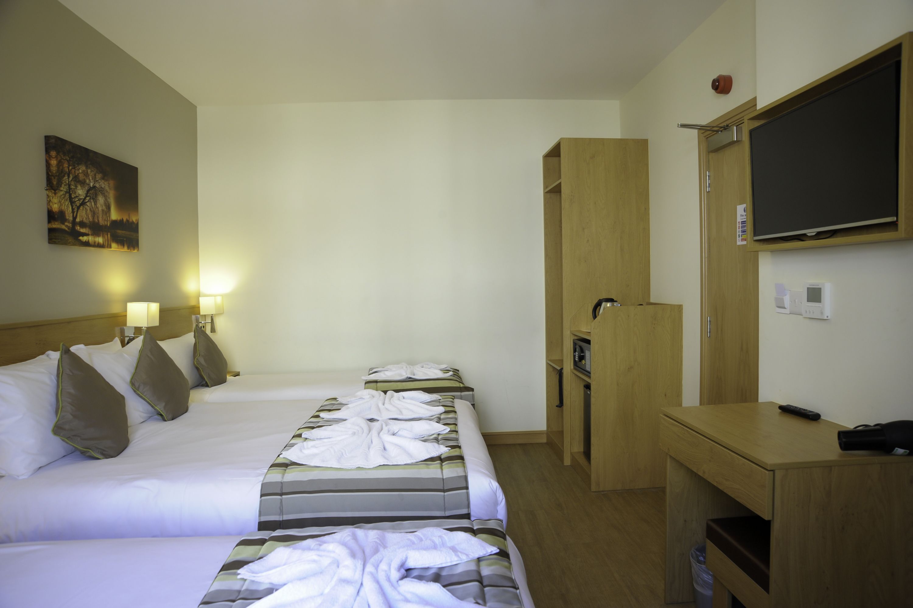 A hotel room with two beds, a desk, a wardrobe, a TV, and a painting on the wall.
