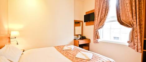 Habitación de hotel con cama, escritorio, televisor y ventana con cortinas.